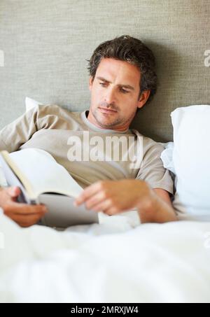 Relaxed man reading book at home. Handsome mature man reading book while lying in bed. Stock Photo
