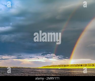 A double rainbow on a rainy day over the Vilyui River against the background of clouds and houses of the village Stock Photo