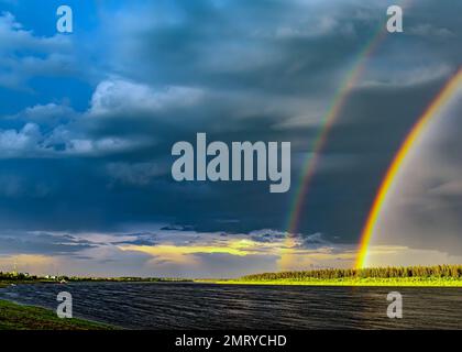 A double rainbow on a rainy day over the Vilyui River against the background of clouds and houses of the village of Suntar in the forest Stock Photo