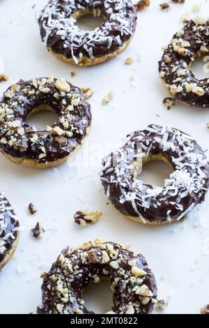 A closeup shot of donuts, with chocolate topping, sprinkled with coconut and chopped walnut, on a white background Stock Photo