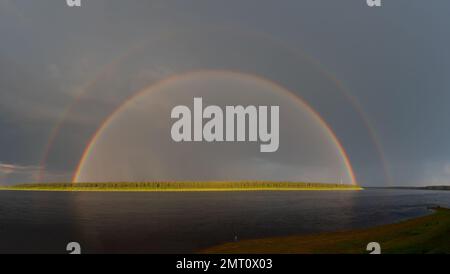 Girl fisherman on the shore. Double rainbow panorama over the Vilyui River after rain against a dark sky with clouds and trees on the shore in Yakutia Stock Photo