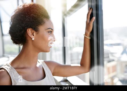 Big dreams require hard work. an ambitious young businesswoman looking through her office window. Stock Photo