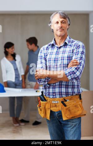 Confident male contractor with clients n background. Portrait of confident male contractor standing with clients discussing in background. Stock Photo