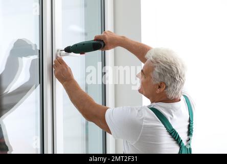 Mature construction worker repairing plastic window with electric screwdriver indoors Stock Photo