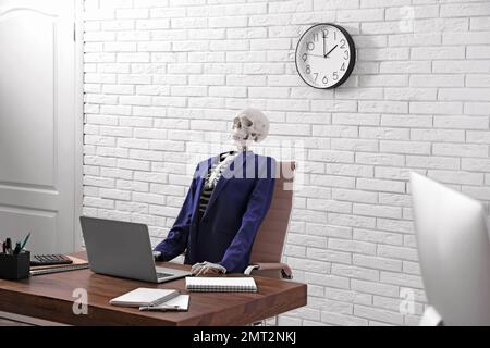 Human skeleton in suit using laptop at table in office Stock Photo