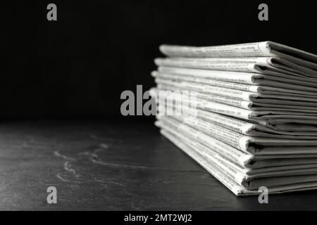 Stack of newspapers on dark stone table, space for text. Journalist's work Stock Photo