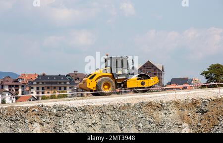 The heavy concrete paver machine on the road against the background of beautiful houses Stock Photo