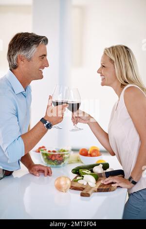 No meal is complete without a toast. an affectionate mature couple toasting with red wine while making dinner. Stock Photo
