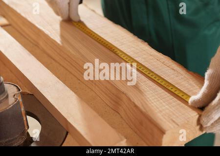 Professional carpenter measuring wooden board at workbench, closeup Stock Photo