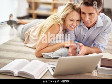 Embracing the digital age together. a mature couple lying on their living room floor doing some online research. Stock Photo