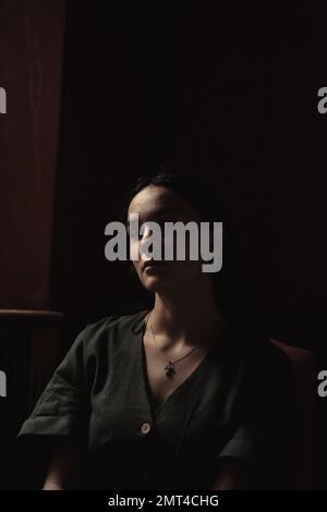 A portrait of a young caucasian woman in a dark room Stock Photo
