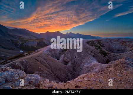 High alpine landscape with craters, mountains and ridges of the French Dauphiné Alps in the distance, seen from the pass Col du Galibier at sunset. Stock Photo