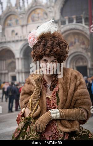 Stylish young lady dressed in opera-cloack, gloves and XIX style dress with a wig on her head and lorgnette in her hand which he is looking through co Stock Photo