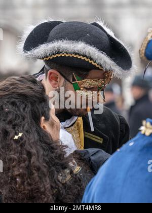 Handsome young man in carnival mask wearing tricorn with an unlit cigarette in his mouth at Venice carnival among his friends Stock Photo