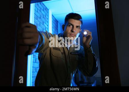 Professional security guard with flashlight checking dark room Stock Photo