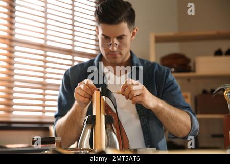 Man making holes in leather belt with stitching awl at workshop Stock Photo