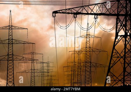 high voltage pylons for electricity and power against sky with dramatic clouds Stock Photo