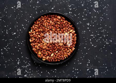 Roasted fresh peanuts in a frying pan on a black background with salt, close up. Stock Photo