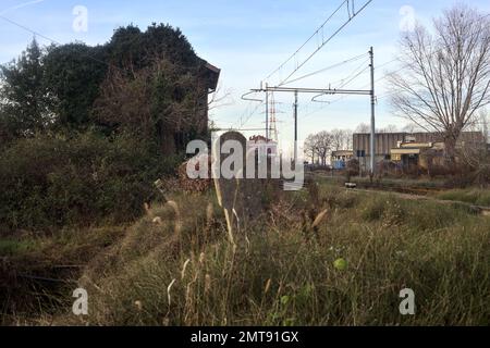 Abandoned  building covered by ivy by the edge of a railroad track on a cloudy day in the italian countryside Stock Photo