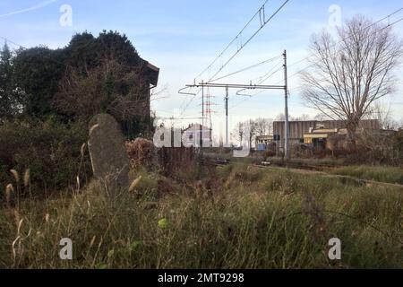 Abandoned  building covered by ivy by the edge of a railroad track on a cloudy day in the italian countryside Stock Photo