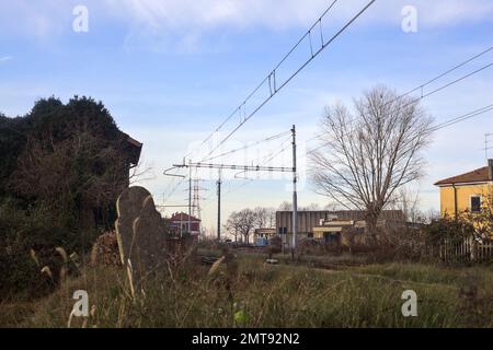 Abandoned  building covered by ivy by the edge of a railroad track on a cloudy day in the italian countryside Stock Photo