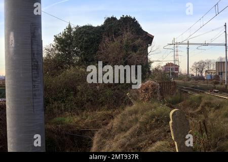 Abandoned  building covered by ivy by the edge of a railroad track on a cloudy day in the italian countryside Stock Photo