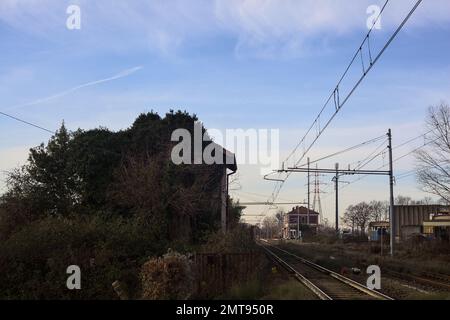 Abandoned  building covered by ivy by the edge of a railroad track on a cloudy day in the italian countryside Stock Photo