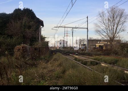 Abandoned  building covered by ivy by the edge of a railroad track on a cloudy day in the italian countryside Stock Photo