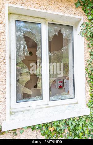 Interior of abandoned Hospital viewed through smashed window hand sanitiser dispenser visible inside and glass shards on window sill outside. Stock Photo