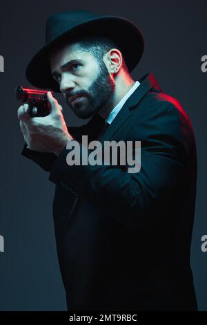 Gangster, suit and shooting gun on dark studio background in secret spy, isolated mafia leadership and crime lord security. Model, man and hitman Stock Photo