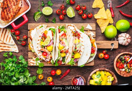 Tacos with grilled chicken, tomato salsa sauce, mango, cilantro and onion in corn tortilla on wooden board. Rustic table background, top view Stock Photo