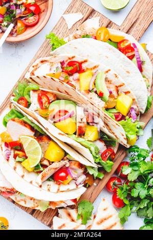 Tacos with grilled chicken, tomato salsa sauce, mango, cilantro and onion in tortilla on cutting board. White table background, top view Stock Photo