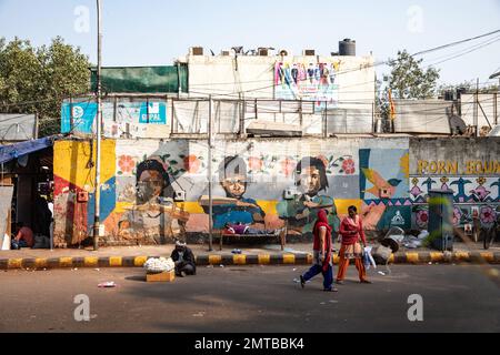 A man taking a nap while two women pass by in a colourful street in in Delhi, India Stock Photo