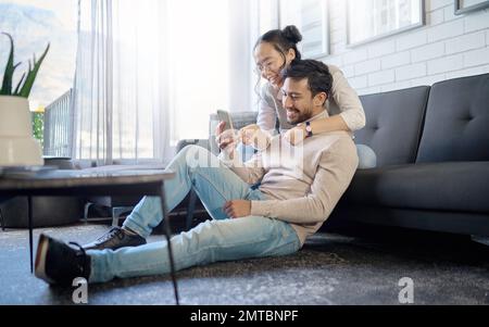 Interracial, couple and people with phone on social media laughing at meme or funny internet content. Man, woman and lovers relax in home, house or Stock Photo