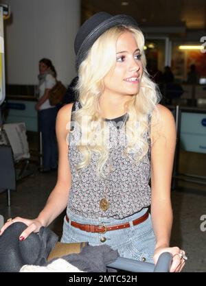 UK singer Pixie Lott shows off her tanned and slightly freckled face as she arrives at Heathrow from LA where she was working on a new album and also attending events including the 2011 Nickelodeon Kids' Choice Awards.  Wearing a trendy fedora with a feather in it, a patterned top paired with striped high-waist short shorts and brown lace-up shoes, Pixie looked happy to be home as she made her way through the airport pushing all her own luggage on a trolly. London, UK. 04/04/11. Stock Photo