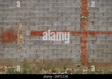 Wall formed by concrete blocks with a cross painted in red spray next to an abandoned lot where weeds grow among the rubble and urban garbage Stock Photo