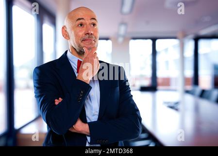 Confident businessman looking thoughtfully while standing in the boardroom. Male professional wearing suit and bow tie. Stock Photo