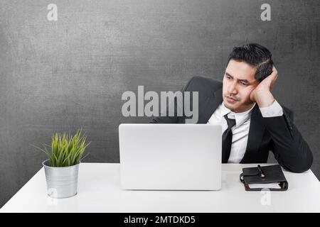 Asian businessman sitting with a laptop on the desk with a tired expression in the office room Stock Photo