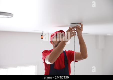 Worker repairing lamp on stretch ceiling indoors Stock Photo