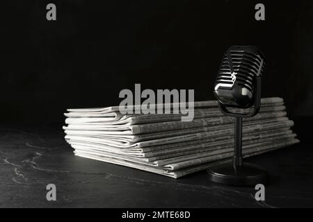 Newspapers and vintage microphone on dark stone table. Journalist's work Stock Photo