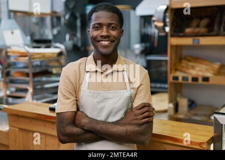 Portrait of happy baker in apron standing with arms crossed and smiling at camera Stock Photo