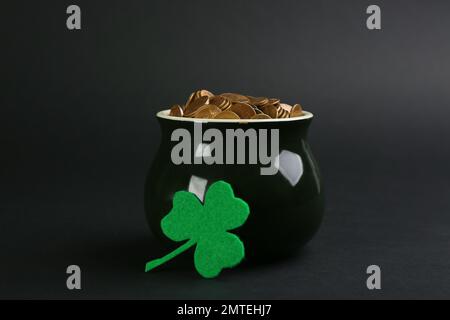Pot of gold coins and clover on black background. St. Patrick's Day celebration Stock Photo