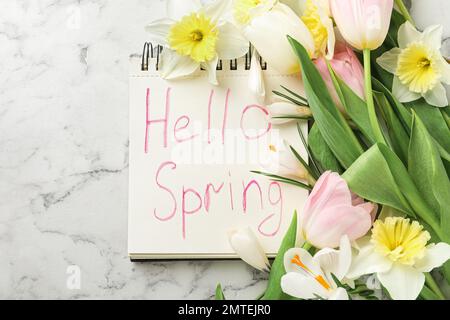 Notebook with words HELLO SPRING and fresh flowers on white marble table, flat lay Stock Photo