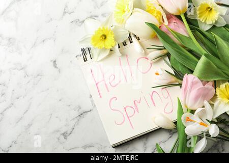 Notebook with words HELLO SPRING and fresh flowers on white marble table, flat lay Stock Photo
