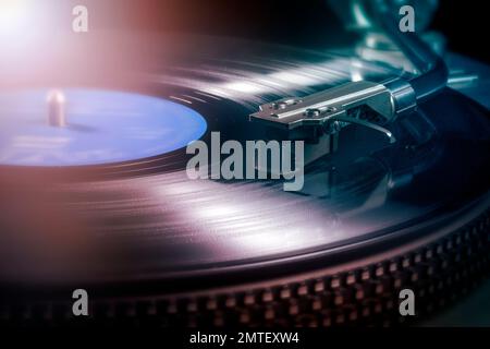 Close up view of turntable capsule playing vinyl record against disco ambiance lights Stock Photo