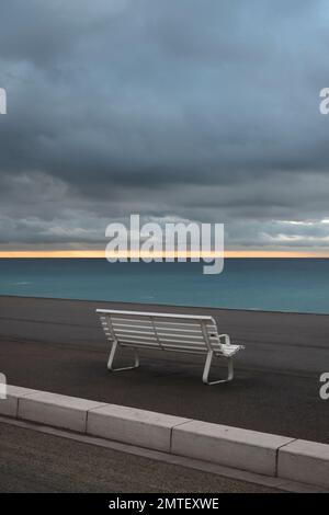 White bench by the sea. Nice Coast at Mediterranean sea.Rising sun at horizon. Romantic concept of promises time. Stock Photo