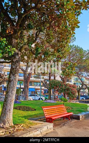 The bright red wooden bench in a beautiful green park on the bank of Lake Maggiore, Locarno, Switzerland Stock Photo