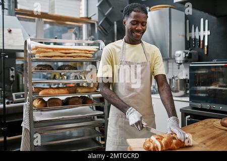 Happy Black baker cutting freshly baked bread in thin slices Stock Photo