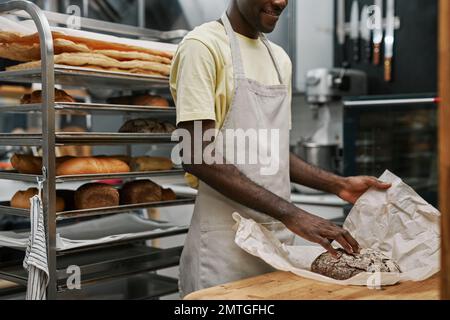 Cropped image of bakery worker wrapping bread in paper for customer Stock Photo