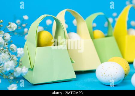 Origami paper baskets and painted quail eggs on a blue background, happy Easter. Stock Photo